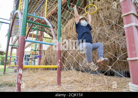 Asiatische Mädchen Kind trägt chirurgische Maske, um die Ausbreitung von Erkältung und Grippe und Viren zu verhindern. Sie haben Spaß und spielen Schleife im Spielplatz im Freien. Stockfoto