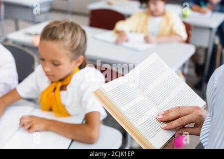 Beschnittene Ansicht des Lehrers Lesebuch in der Nähe der Schüler im Klassenzimmer Stockfoto