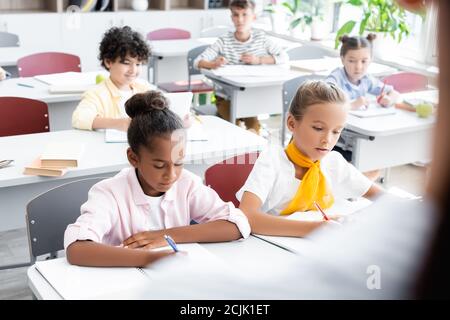 Selektiver Fokus auf multikulturelle Schüler, die während des Unterrichts in Notizbüchern schreiben Stockfoto
