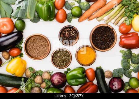 Draufsicht auf frisches reifes Gemüse und Obst rund um Schalen Mit Gewürzen auf weißem Hintergrund Stockfoto