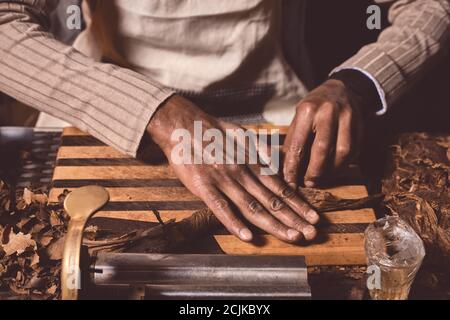 Nahaufnahme von Männerhänden, die Zigarren aus Tabakblättern machen. Traditionelle Herstellung von Zigarren. Demonstration der Herstellung von handgefertigten Zigarren. Hände Rollen Stockfoto