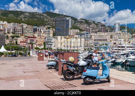 Monte Carlo, Monaco - 15. August 2018: Geparkte Roller stehen in Port Hercule, Touristen gehen die Straße von Monaco Stadt Stockfoto