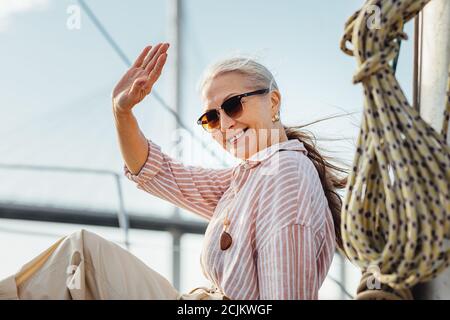 Glückliche Frau trägt Sonnenbrille winkt ihre Hand und Blick auf Kamera Stockfoto