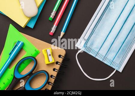 Schulbedarf und eine medizinische Maske auf dem Tisch, Draufsicht. Konzept zum Thema Masken in Bildungseinrichtungen Stockfoto