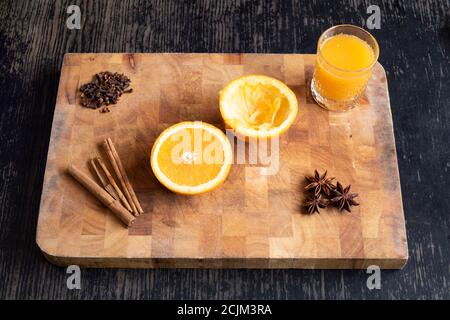 Gewürzte Orange – ein frisch geschnittenes und gepresstem Glas Orangensaft mit aromatischen Gewürzen Zimt, Nelken und Sternanis auf einem Holzschneidebrett Stockfoto