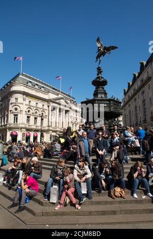 Touristen sitzen am Fuße des Shaftesbury Memorial Fountain, auch bekannt als Eros, im Piccadilly Circus, London, England. Stockfoto