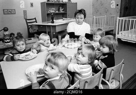 15. November 1984, Sachsen, Wildenhain: Im November 1984 sitzen Kinder mit ihrer Lehrerin in einem Kindergarten in Wildenhain bei Eilenburg beim Essen am Tisch. Genaues Datum der Aufnahme nicht bekannt. Foto: Volkmar Heinz/dpa-Zentralbild/ZB Stockfoto