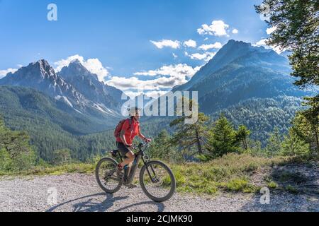 Nette und aktive ältere Frau, die ihr elektrisches Mountainbike reitet Auf einer alten Militärstraße von Toblach bis zum Gipfel der Marchkinkele eith spektakulär Stockfoto