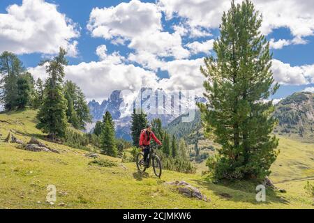 Nette und aktive ältere Frau auf ihrem elektrischen Mountainbike auf dem Hochplateau von Prato Piazzo in den drei Gipfeln Dolomiten, felsige Silhouette Stockfoto