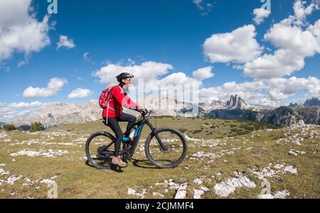 Nette ältere Frau, die mit ihrem Elektro-Mountainbike unter dem berühmten drei Gipfel des Lavaredo in den Sexten Dolomiten in Südtirol, Italien, fährt Stockfoto