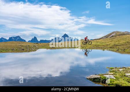 Nette Frau, die mit ihrem elektrischen Mountainbike die drei Zinnen Dolomiten fährt und sich im blauen Wasser eines kalten Bergsees spiegelt Stockfoto