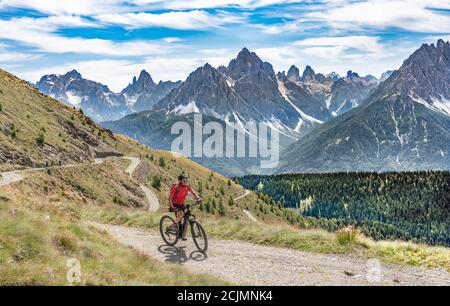 Nette und aktive ältere Frau, die ihr elektrisches Mountainbike reitet Auf einer alten Militärstraße von Toblach bis zum Gipfel der Marchkinkele eith spektakulär Stockfoto
