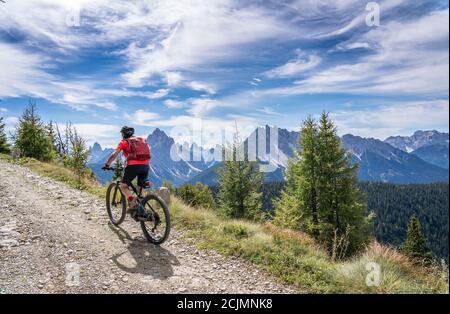 Nette und aktive ältere Frau, die ihr elektrisches Mountainbike reitet Auf einer alten Militärstraße von Toblach bis zum Gipfel der Marchkinkele eith spektakulär Stockfoto