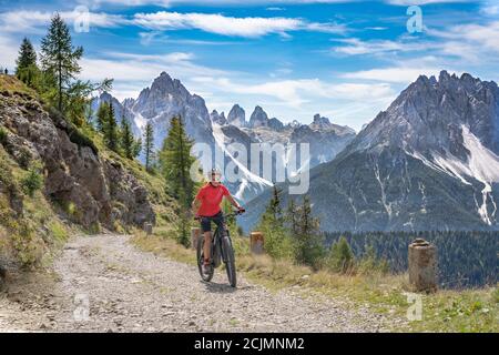 Nette und aktive ältere Frau, die ihr elektrisches Mountainbike reitet Auf einer alten Militärstraße von Toblach bis zum Gipfel der Marchkinkele eith spektakulär Stockfoto