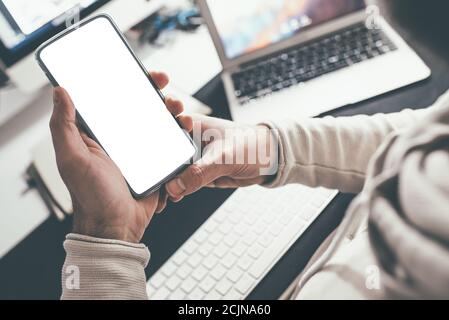 Über die Schulter Blick der Person hält Smartphone mit blank Weißer Touchscreen am Schreibtisch Stockfoto