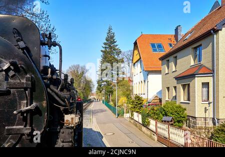 Häuser in den Straßen der Stadt Wernigerode mit einer vorbeifahrenden Dampflokomotive. Dynamisch durch Bewegungsunschärfe. Stockfoto