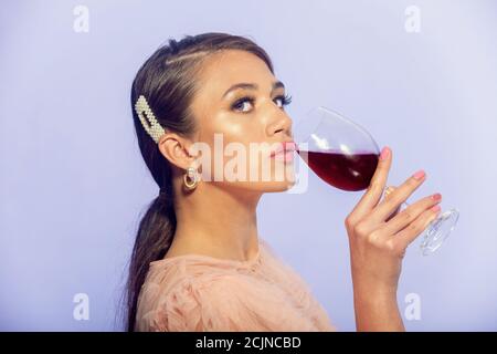 Eine junge Frau, die ein Glas Rotwein in sich hält Ihre Hand gegen einen schlichten Studiohintergrund Stockfoto