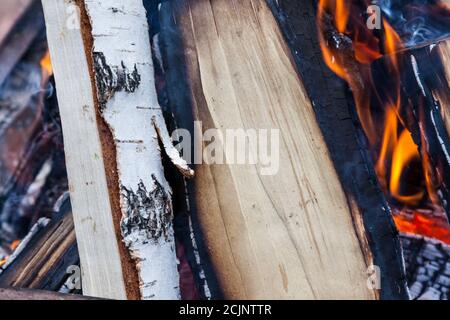 Nahaufnahme von hölzernen Birkenstämmen auf Feuer in einem Kamin oder Lagerfeuer in Zungen von oranger Flamme beim Kochen auf einem offenen Feuer. Ein gemütlicher Abend an Weihnachten Stockfoto