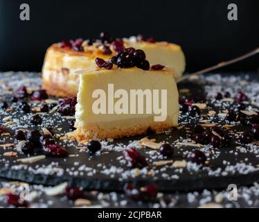 Gourmet-Käsekuchen mit Heidelbeeren und Preiselbeere serviert auf einem dunklen Platte mit dunklem Hintergrund Stockfoto