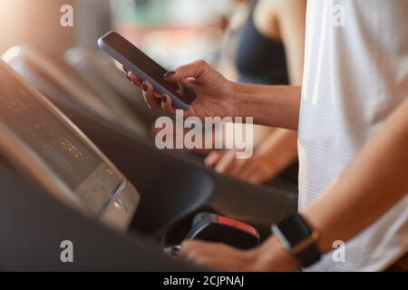 Nahaufnahme einer Frau, die während des Trainings ihr Mobiltelefon benutzt Laufband im Fitnessstudio Stockfoto