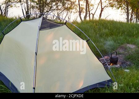 Camping Zelt Markise auf dem Gras in der Nähe des Flusses, ein Feuer brennt, der Kessel wärmt. Stockfoto