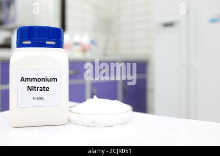 Selektiver Fokus einer Flasche Ammoniumnitrat in einer Plastikflasche neben einer Petrischale mit weißen Pellets im Laborhintergrund. Stockfoto