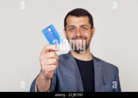 Junger Geschäftsmann Mann mit Bart lächelnd, hält Kreditkarte mit glücklichen Gesicht, stehend und lächelnd mit selbstbewussten Lächeln, zeigt Zähne. Stockfoto