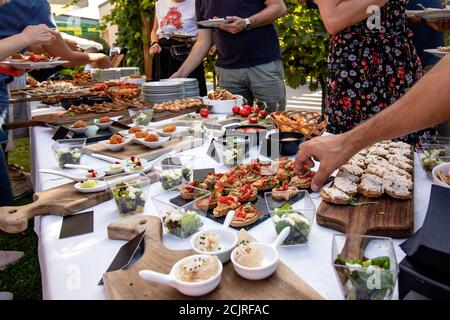 Gartenparty im Freien mit Buffettisch voller Canapes. Menschen, die sich selbst dienen. Nahaufnahme der Hände, die Fingernahrung in ihre Teller nehmen. Stockfoto