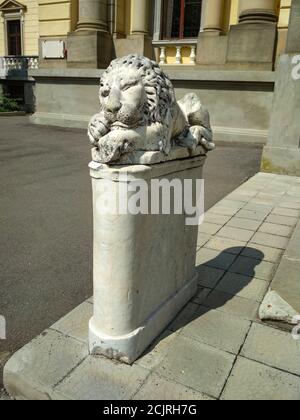 Statue eines steinernen Löwen, der auf einem Sockel schläft Vor einem alten Herrenhaus Stockfoto