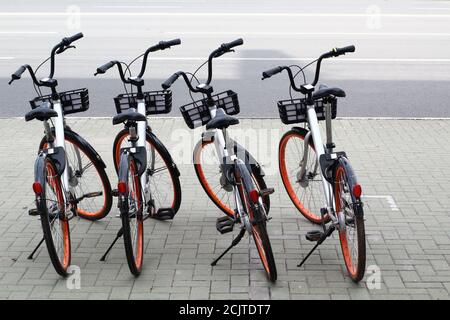 Fahrräder, die in Reihe bei einem Fahrradverleih in einem Fahrradladen auf einer Straße geparkt werden. Stadtfahrrad öffentlichen Parkplatz mieten. Teilen Fahrräder Sattel. Stockfoto