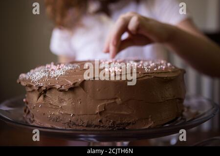 Nahaufnahme der Hand eines Kindes Dekorieren einer Schokolade Frosted Geburtstagskuchen mit Streuseln Stockfoto