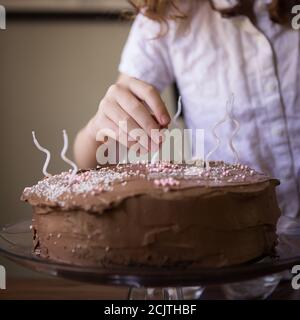 Ein junges Kind dekorieren eine Schokolade Frosted Geburtstagstorte mit Weiße Kerzen Stockfoto