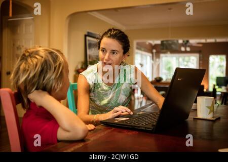 Eine Mutter hilft ihrem kleinen Sohn bei der Heimsschoolung vor einem Laptop, während sie Fernunterricht an einem Tisch zu Hause in Miami, Florida, USA, macht Stockfoto