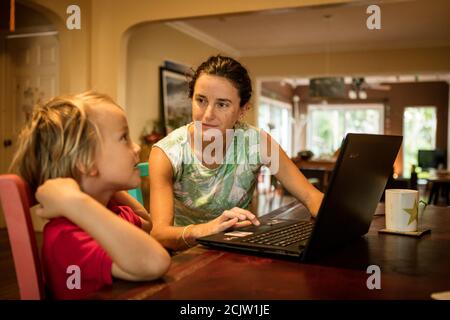 Eine Mutter hilft ihrem Jungen bei der Heimschoolung vor einem Laptop, während sie zu Hause am Tisch in Miami, Florida, USA, Fernunterricht macht Stockfoto