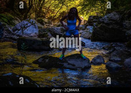 Frau Silhouette am Flussufer im Sonnenaufgang. Waldbach mit Felsen. Stockfoto