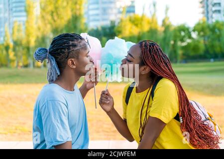 Ein glückliches schwarzes Paar, das bunte Zuckerwatte zusammen in einem Park einer großen Stadt hat. Stockfoto