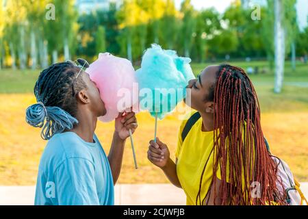 Ein glückliches schwarzes Paar, das bunte Zuckerwatte zusammen in einem Park einer großen Stadt hat. Stockfoto