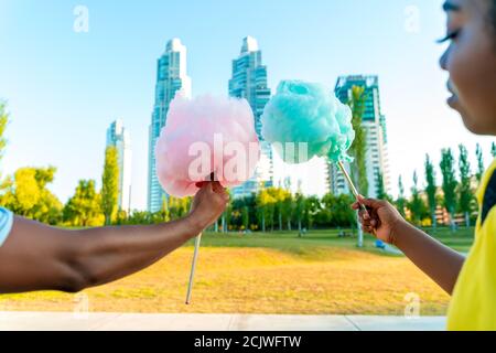 Ein glückliches schwarzes Paar, das bunte Zuckerwatte zusammen in einem Park einer großen Stadt hat. Stockfoto