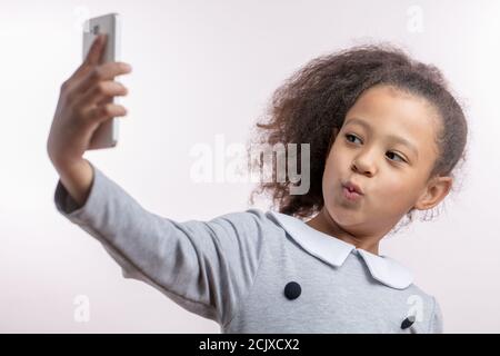 Lustige afrikanische Mädchen nimmt ein Selfie. Gadget-Konzept. Freizeit. Unterhaltung mit Smartphone. Kind mag Selfies Stockfoto