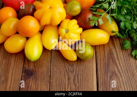 Verschiedene Sorten von Tomaten und ein Bündel von grüner Petersilie auf einem hölzernen Hintergrund. Stockfoto