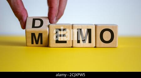Hand dreht einen Würfel und ändert das Wort 'Demo' auf Holzwürfel in 'Demo'. Schöner gelber Tisch, weißer Hintergrund, Kopierraum. Stockfoto