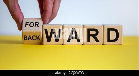 Hand dreht einen Würfel und ändert das Wort "rückwärts" auf "vorwärts" auf Holzwürfeln. Schöner gelber Tisch, weißer Hintergrund, Kopierraum. Stockfoto