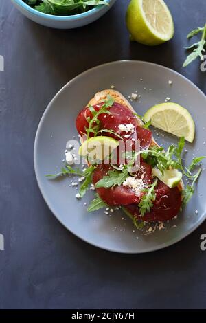 Brotscheibe mit Bresaola, Rucola und Parmesan isoliert auf grauem Hintergrund. Nahaufnahme. Gesunde Ernährung Konzept. Stockfoto