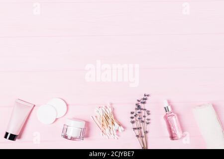 Arrangement mit Beauty-Produkten, Creme, Lotion, Aromaöl, Baumwollpads und Lavendelblüten auf rosa Hintergrund mit Kopierfläche. Stockfoto