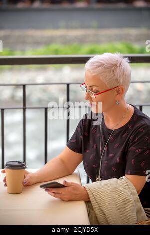 Blonde Frau, die auf die Kunststoff-Tasse Cappuccino. Seitenansicht Foto. Stockfoto
