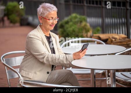 Eine ältere Frau spricht von Skype Witz einem Freund am Street Coffee Shop. Seitenansicht Foto. alte Menschen Konzept Stockfoto