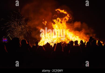 Menschen in Silhouette stehen und beobachten ein großes Lagerfeuer bei den jährlichen Guy Fawkes & Bonfire Night Feiern in Littlehampton, West Sussex, Großbritannien. Stockfoto
