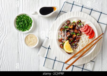 Japanische Teriyaki gebackenen Tofu mit Reis bestreut von Frühlingszwiebeln, Sesam mit Reis serviert, Tomate in Scheiben geschnitten, Zitrone auf einer weißen Schüssel mit Essstäbchen Stockfoto