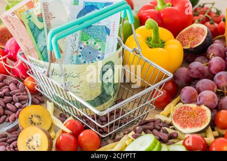 Einkaufskorb mit iranischem Geld, rund um Lebensmittel, Gemüse und Obst. Das Konzept der Inflation, steigende Preise und teurere Lebensmittel Stockfoto