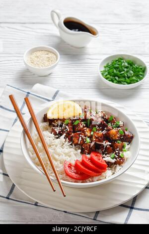 Teriyaki gebackenen Tofu mit Reis bestreut von Frühlingszwiebeln, Sesam, japanische Küche, serviert mit Reis, Tomate, Zitrone auf einer weißen Schüssel mit c Stockfoto